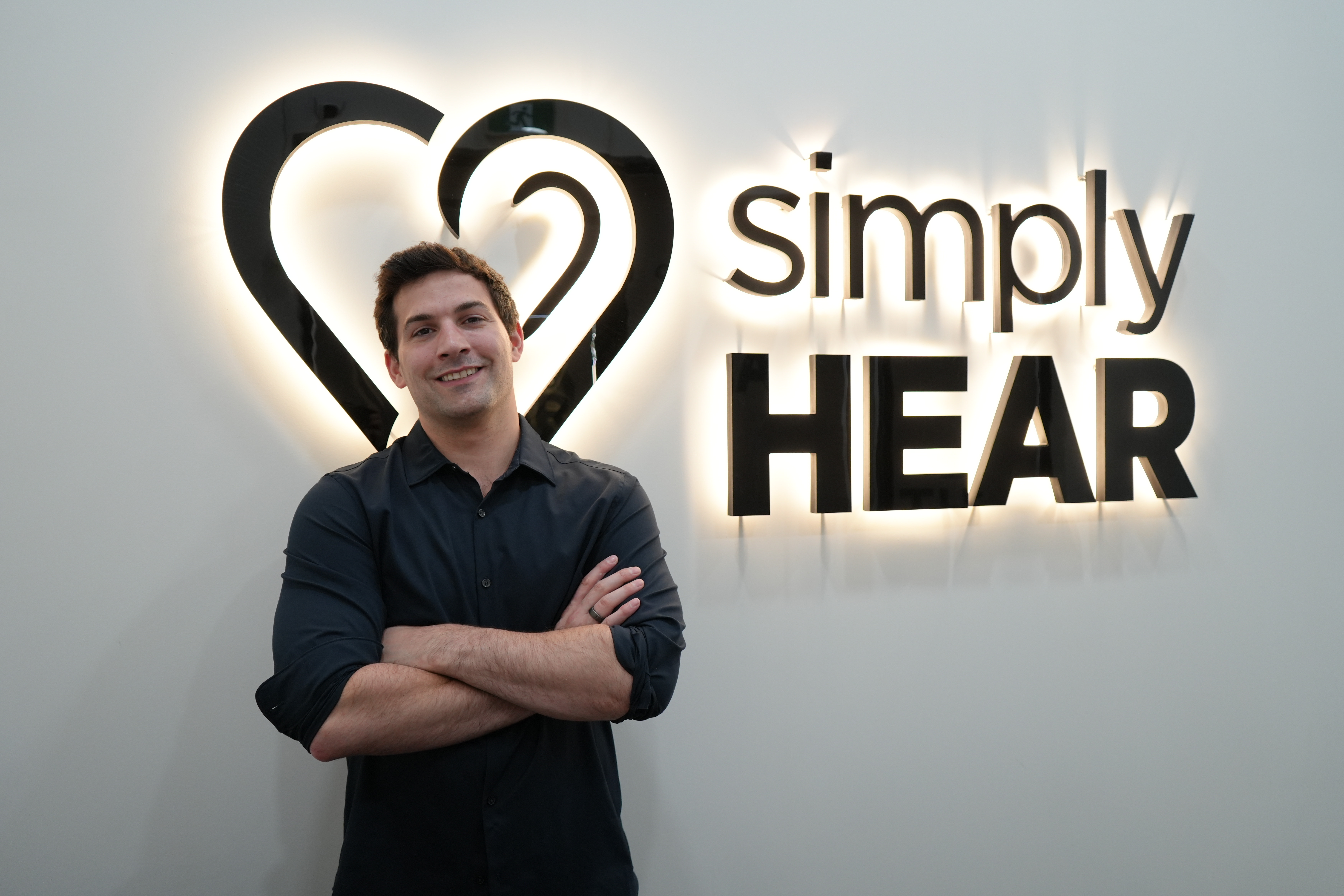 Armando Di Lello, founder of simplyHEAR, standing in front of the simplyHEAR logo